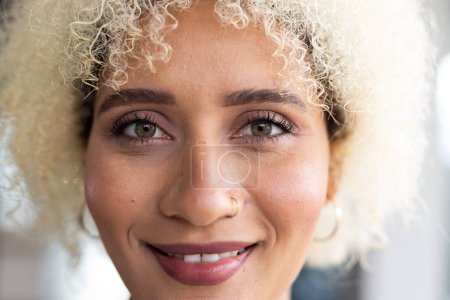 In modern office, biracial young female with curly blonde hair, smiling. 