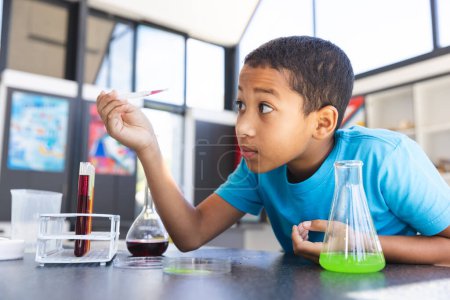 Biracial boy engaged in a science experiment at school in the classroom. His curiosity is evident as he observes the chemical reaction with interest.