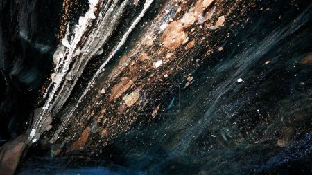 Téléchargez les photos : The black transparent color of ice in the cave. Small stones hang down in places. There are frozen air bubbles and grains of sand in the ice. Black-brown shade of ice. Deep in the glacier. Epic - en image libre de droit