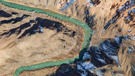 Téléchargez les photos : Une longue rivière avec de l'eau verte dans le canyon Charyn. Il y a de la neige blanche par endroits. Les buissons et les arbres poussent. La rivière traverse un canyon entre les rochers et les falaises. Les montagnes sont visibles. Vue sur drone - en image libre de droit