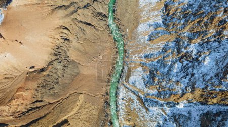 Téléchargez les photos : Une longue rivière avec de l'eau verte dans le canyon Charyn. Il y a de la neige blanche par endroits. Les buissons et les arbres poussent. La rivière traverse un canyon entre les rochers et les falaises. Les montagnes sont visibles. Vue sur drone - en image libre de droit