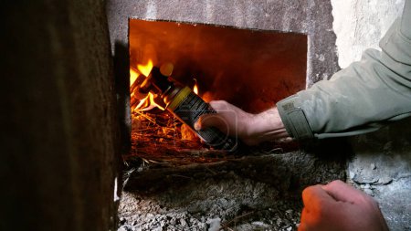 Photo for The guy lights a fire in the oven. To lay firewood. An old stove in an abandoned hut. Rusty metal doors. Dirty dusty walls. Firewood and fuel briquettes are burning. Heat from the oven. - Royalty Free Image
