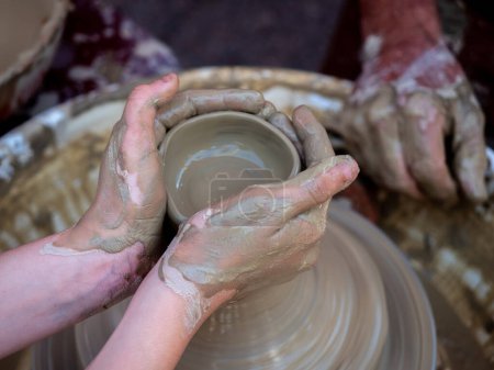 Photo for Potter helps a girl with his hands to create a clay pot on the lathe - Royalty Free Image