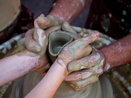 Photo for Potter helps a girl with his hands to create a clay pot on the lathe - Royalty Free Image