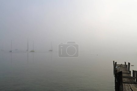 Foto de Algunos barcos de vela en la luz de fondo en el lago Ammersee en la niebla de la mañana - Imagen libre de derechos
