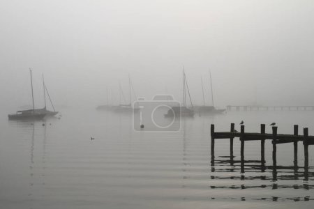 algunos barcos de vela en la luz de fondo en el lago Ammersee en la niebla de la mañana