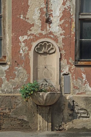 Téléchargez les photos : Une vieille fontaine d'eau devant la façade d'un bâtiment en décomposition - en image libre de droit