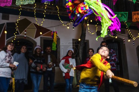 Familia hispana rompiendo una piñata en tradicional celebración de posada mexicana por Navidad en México América Latina