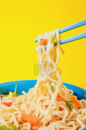 Instant noodles ramen soup on bowl and chopsticks on yellow background