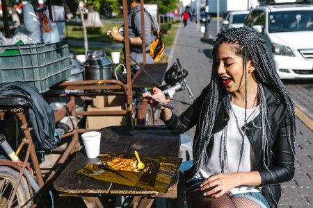 young latin woman with braids hair eating mexican tamales street food on park in Mexico city, hispanic people