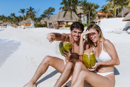 Photo for Hispanic young couple holding a coconut and having fun on caribbean beach in holidays or vacations in Mexico Latin America - Royalty Free Image