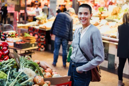 Foto de Mujer joven hispana con cabeza rapada o pelo corto comprando verduras en el mercado tradicional o en la tienda de comestibles - Imagen libre de derechos