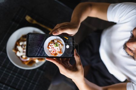 latin man using smartphone to take photos of food on the table at home in Mexico Latin America
