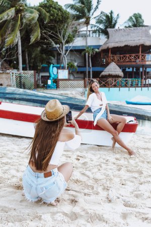 joven mujer latina tomando foto selfie con teléfono móvil a amiga en la playa caribeña en México América Latina, mujer hispana