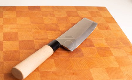On a wooden board lies a Japanese Nakiri kitchen knife with a wooden handle.