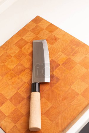 Auf einem Holzbrett liegt ein japanisches Nakiri-Küchenmesser mit Holzgriff.