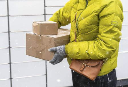 Photo for A woman with a box in his hands near the self-service mail terminal. Parcel delivery machine. Person holding a cardboard box. Mail delivery and post service, online shopping, e commerce concept - Royalty Free Image