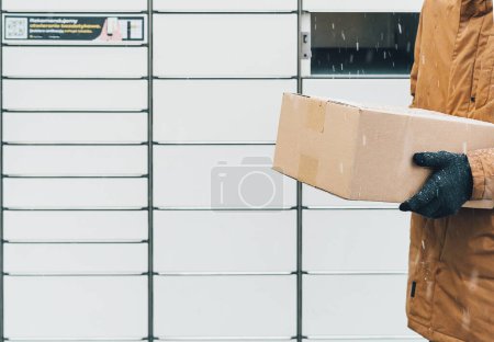 Photo for A man with a box in his hands near the self-service mail terminal. Parcel delivery machine. Person holding a cardboard box. Mail delivery and post service, online shopping, e commerce concept - Royalty Free Image