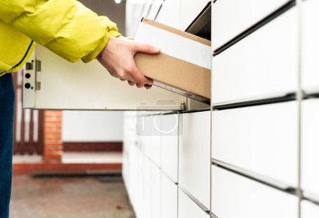 Photo for A woman with a box in his hands near the self-service mail terminal. Parcel delivery machine. Person holding a cardboard box. Mail delivery and post service, online shopping, e commerce concept - Royalty Free Image