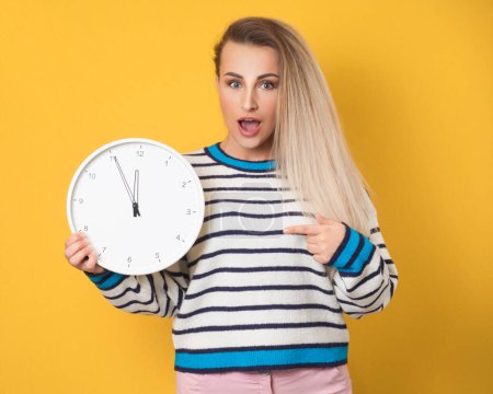 Photo for Hurry up concept. Surprised woman holding wall clock and pointing to timer, isolated on yellow background. Amazed girl with wall clock. Studio shot - Royalty Free Image