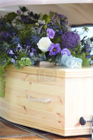 Photo for Close Up Of Plain Wooden Coffin With Floral Tributes In Back Of Hearse At Funeral - Royalty Free Image