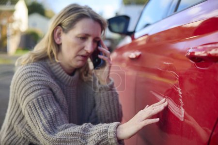 Foto de Conductor femenino maduro infeliz con coche dañado después del accidente que llama a la compañía de seguros en el teléfono móvil - Imagen libre de derechos