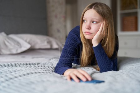 Adolescente infeliz con teléfono móvil acostada en la cama en casa ansiosa por el acoso en línea en las redes sociales y el uso excesivo del teléfono