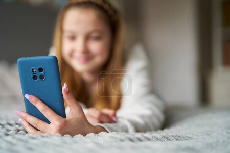 Smiling Teenage Girl With Painted Nails Lying On Bed At Home Using Mobile Phone