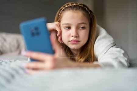 Adolescente infeliz con teléfono móvil acostada en la cama en casa ansiosa por el acoso en línea en las redes sociales y el uso excesivo del teléfono 
