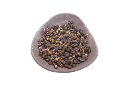 Foto de Baya de lobo negro, también llamada baya de goji negro. Estas bayas se utilizan como té de hierbas en la medicina tradicional china. Hierbas secas en plato de arcilla, enfoque selectivo aislado sobre fondo blanco - Imagen libre de derechos