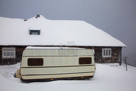 Foto de Camper - a small van for lovers of trips to nature near old mountain snow-covered hut. Meteorological observatory on Mount Pozhyzhevska - Imagen libre de derechos