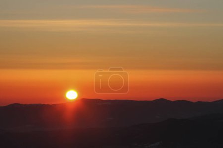 Orange sky and sun disc at sunrise in dark winter mountains, Carpathians