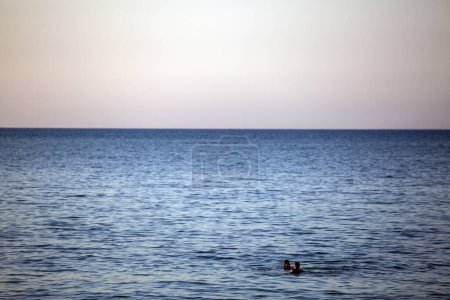 Photo for A man and a woman swimming in the ocean in front of the yellow evening sky. Vacation on the Adriatic sea - Royalty Free Image