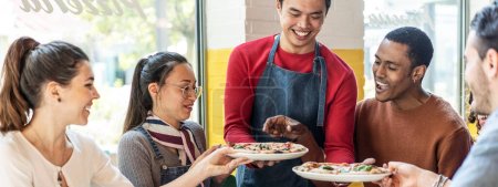Photo for Horizontal banner or header with waiter serving delicious pizzas margherita to multicultural friends in cozy pizzeria restaurant - Multiethnic friends having fun together at the pizzeria - Royalty Free Image