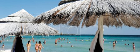 Photo for Horizontal banner or header with a beautiful beach resort with straw umbrellas on a blue sky and white clouds. On the background bathers  in swimsuits. Beach life and lifestyle concept. - Royalty Free Image