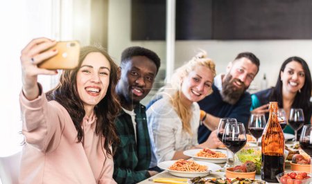 Photo for Multiethnic guys and women taking selfie for lunch in the home kitchen - Young friends having fun together in the apartment while eating delicious italian spaghetti with tomato sauce - Bright filter - Royalty Free Image