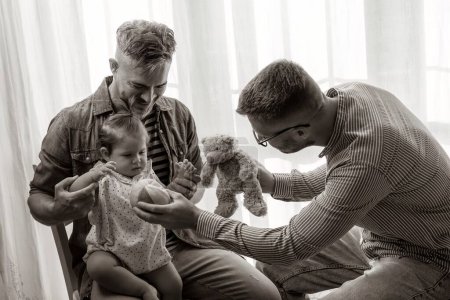 Téléchargez les photos : Couple gay masculin avec bébé adopté à la maison - Deux beaux pères jouant avec leur fille - Famille Lgbtq + à la maison - Concept de diversité et relation familiale LGBTQ - Montage noir et blanc - en image libre de droit