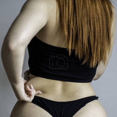 Overweight young redhead woman wearing black lingerie holding fat with hand on right side - Body acceptance concept - Body positive