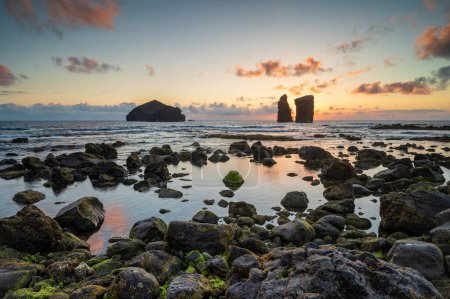 Foto de Increíble puesta de sol en la playa de Mosteiros con sus islotes, Azores Sao Miguel isla, Portugal. Paisaje al atardecer sobre el mar en las costas en una hermosa noche de verano. Paisaje marino. - Imagen libre de derechos