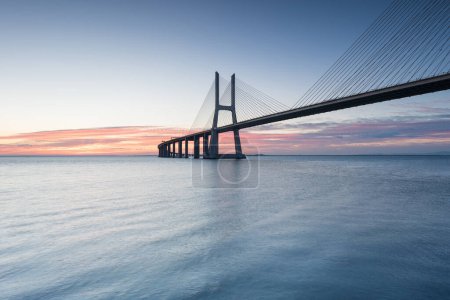 Foto de Fondo con colorido amanecer en el puente de Lisboa. El puente Vasco da Gama es un hito, y uno de los puentes más largos del mundo. Paisaje urbano. Portugal es un destino turístico increíble. - Imagen libre de derechos