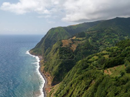 Foto de Amazing landscape on the northeast coast of the island of Sao Miguel in the Azores. Panoramic view of the cliff with a path to the sea and a small fishing port. Tourist attraction of Portugal. - Imagen libre de derechos