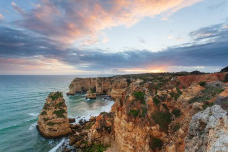 Téléchargez les photos : Paysage sur la côte de l'Algarve au coucher du soleil. Plage dans le sud du Portugal la meilleure destination de voyage pour les touristes en vacances. Paysage marin avec grottes à travers les falaises - en image libre de droit