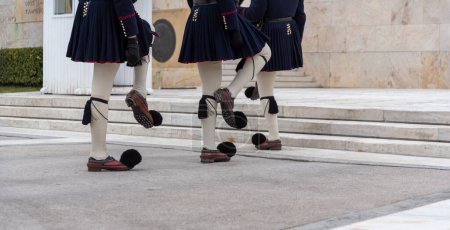 Photo for Text on the wall "And one bed remains empty for the unknown" in Greek and greek evzone soldiers in traditional costumes guard of honor at a monument in greece - Royalty Free Image