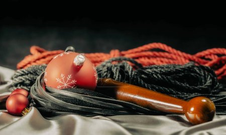 Foto de Bdsm naturaleza muerta látigo de cuero negro y bolas de Navidad rojas en tela de plata - Imagen libre de derechos