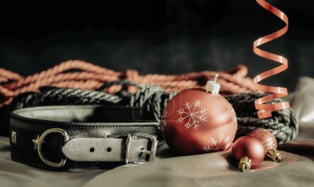 Foto de Bdsm bodegón collar de cuero negro y bolas de Navidad rojas en tela de plata de cerca - Imagen libre de derechos