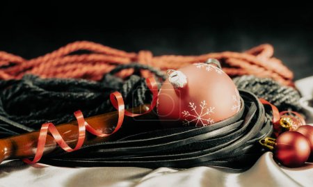 bdsm still life black leather whip and red christmas balls on silver fabric close up