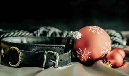 Foto de Bdsm bodegón collar de cuero negro y bolas de Navidad rojas en tela de plata de cerca - Imagen libre de derechos