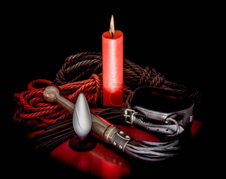 Téléchargez les photos : Corde bdsm avec une bougie rouge et un fouet avec un collier en cuir sur un fond sombre - en image libre de droit