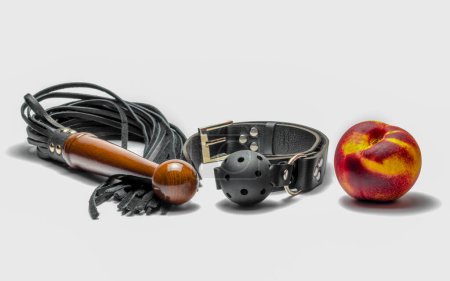 Foto de Bdsm cuero negro mordaza látigo y fruta madura del melocotón sobre fondo blanco - Imagen libre de derechos
