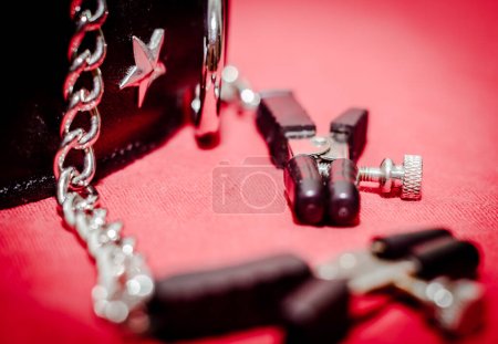 Foto de Bdsm accesorio collar humano y accesorio broche de pezón con cadena metálica sobre fondo rojo de cerca - Imagen libre de derechos